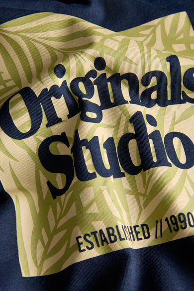 Blauw T-shirt met korte mouwen van ORIGINALS BY JACK & JONES, met een tropisch bladerenpatroon en de tekst 'Originals Studio Established // 1990'.