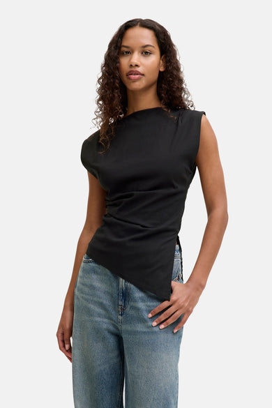 Zwarte blouse zonder mouwen van JJXX, met asymmetrische zoom en gedragen met blauwe jeans.
