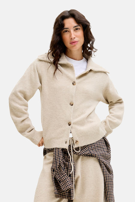 Beige vest van JJXX, gedragen over een wit T-shirt en een geruite blouse om de taille.