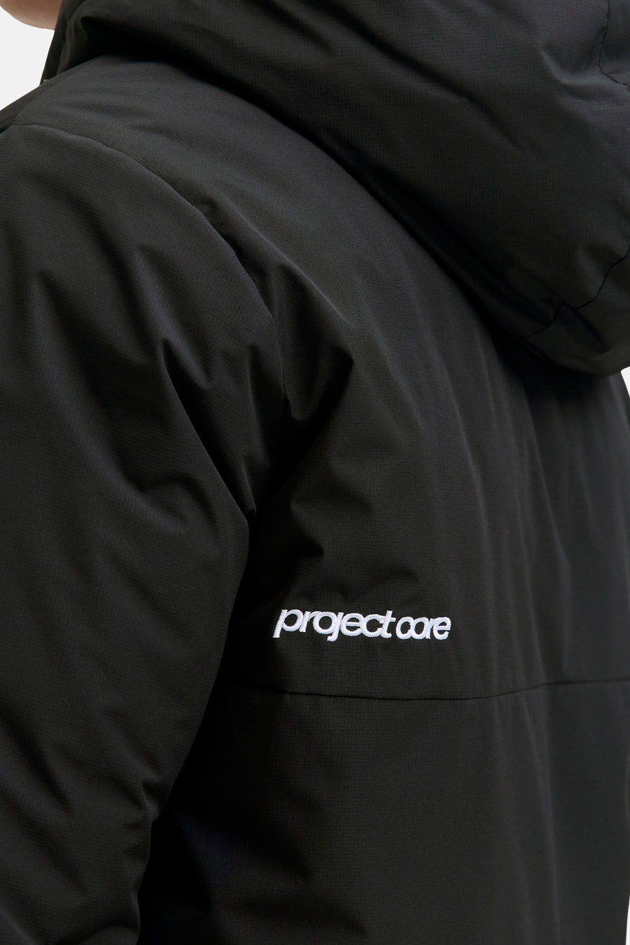 Zwarte korte jas van CORE BY JACK & JONES met subtiele ripstop textuur, capuchon en wit "project core" borduursel.