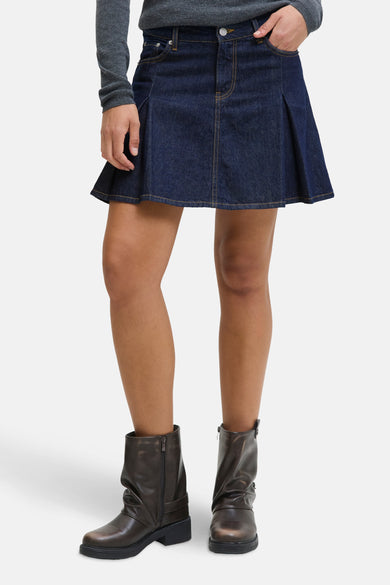 Short skirt of dark blue denim from JJXX, with pleats and brown stitching, combined with brown trousers.