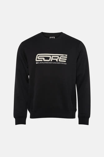 Pull noir de CORE BY JACK & JONES, avec impression de logo blanc, porté avec un jean bleu déchiré et des baskets grises.