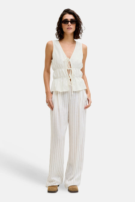 Witte mouwloze blouse van JJXX met striksluiting en peplumzoom, gedragen met gestreepte broek en zonnebril.