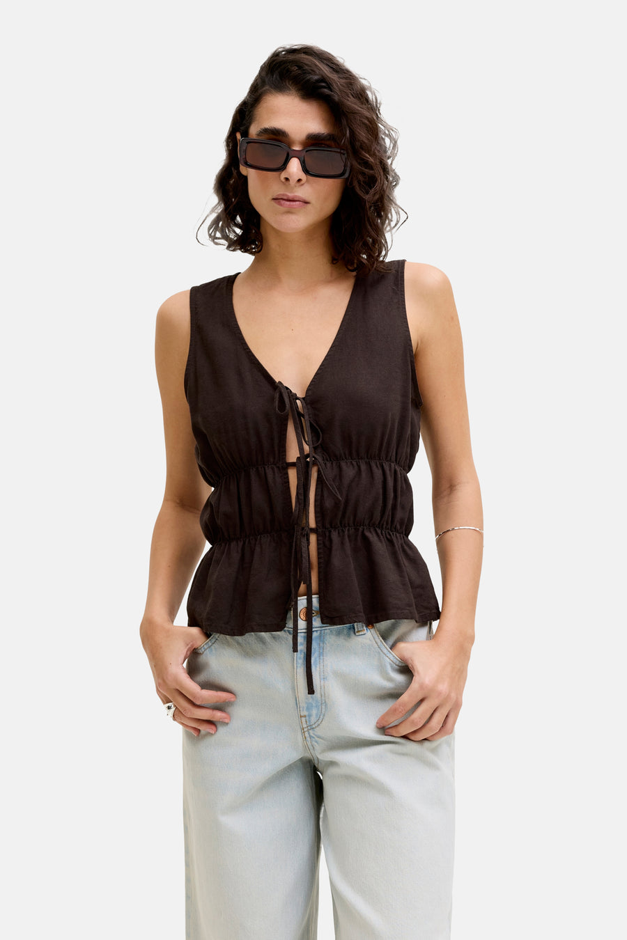 Bruine mouwloze blouse van JJXX met V-hals en striksluiting, gecombineerd met lichte jeans en zonnebril.