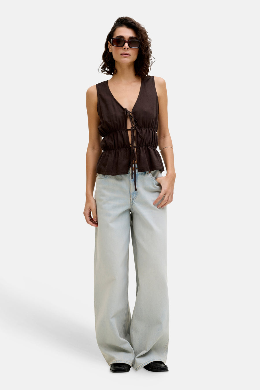 Mouwenloze bruine blouse van JJXX met strikjes aan de voorkant, gedragen met een wijde jeans en loafers.