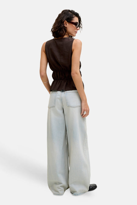 Bruine mouwloze blouse van JJXX met peplumzoom en elastische taille, gecombineerd met wijde lichtblauwe jeans, van achteren gezien.