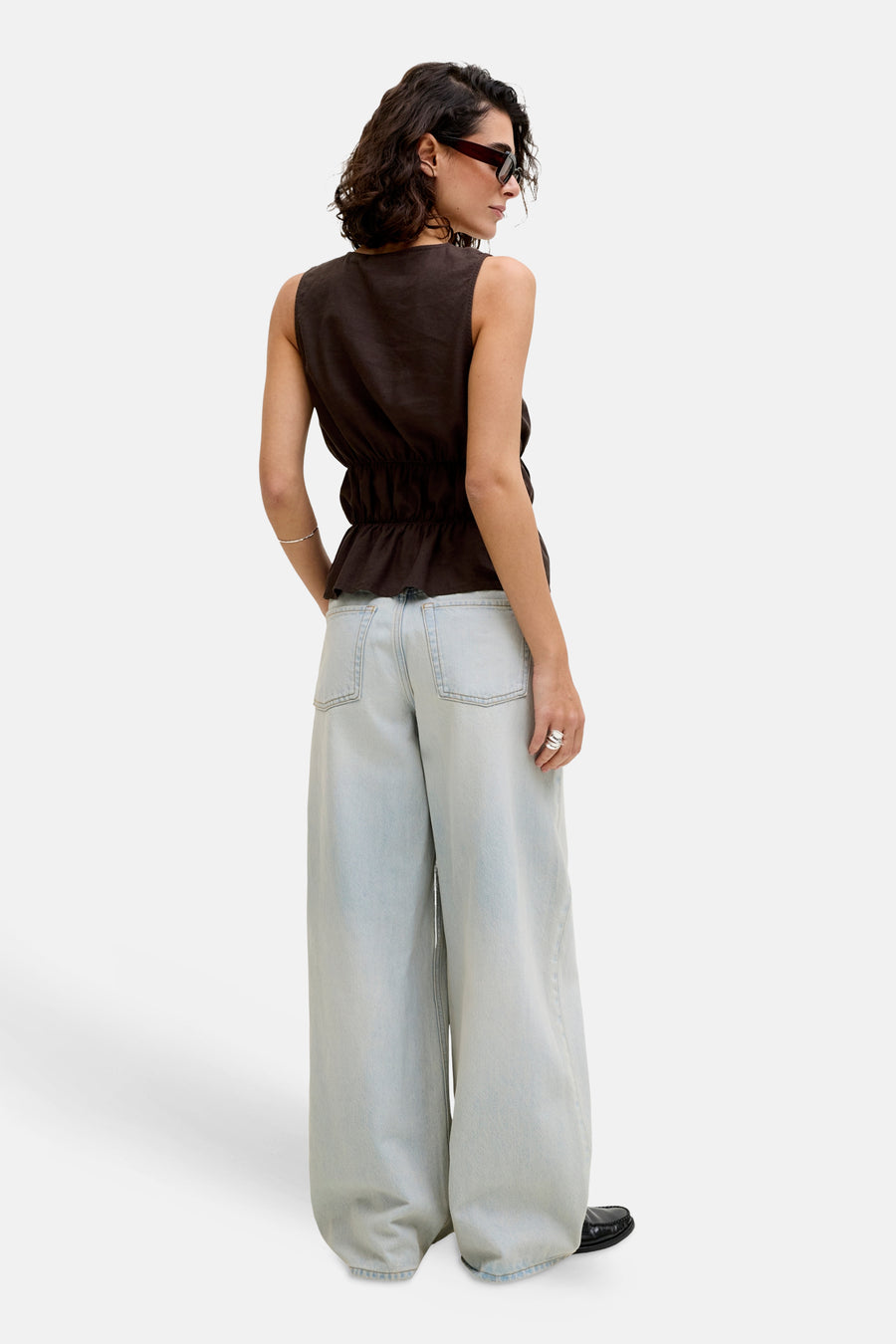 Bruine mouwloze blouse van JJXX met peplumzoom en elastische taille, gecombineerd met wijde lichtblauwe jeans, van achteren gezien.