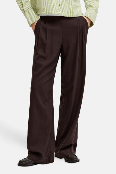 Bruine broek van JJXX, met wijde pijpen en plooien aan de voorkant, gedragen met een groen geruite blouse.
