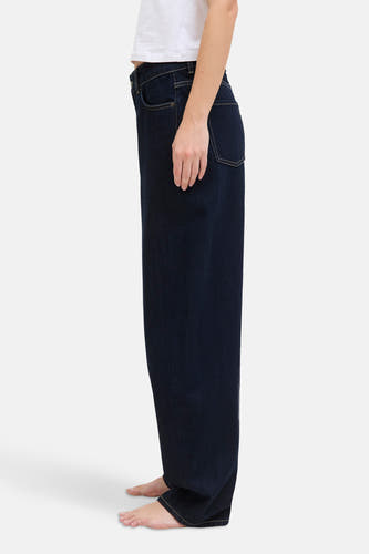 Jean en denim bleu marine avec une forme spéciale de JJXX, en vue latérale et porté avec un haut blanc.