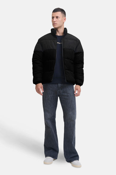 Zwarte korte jas van CORE BY JACK & JONES, met een gewatteerd ontwerp, gedragen met donkere jeans en witte sneakers.
