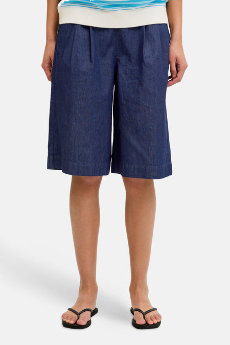 Donkerblauwe denim shorts van JJXX, met plooien aan de taille, gedragen met een gestreept shirt en slippers.
