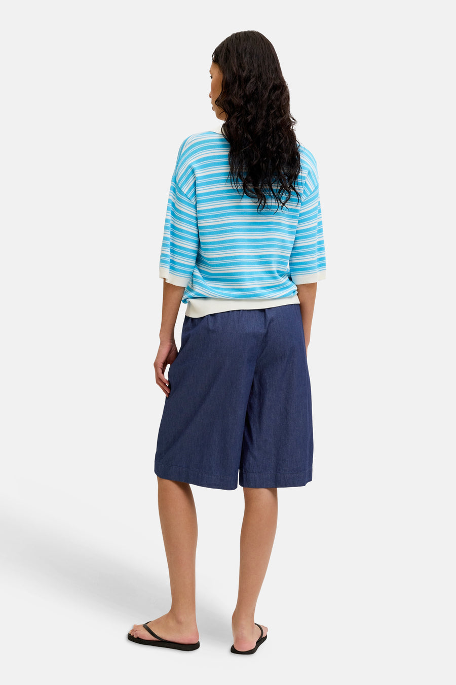 Donkerblauwe denim short van JJXX, wijd model, knielengte, achterkant, gedragen met gestreept shirt en zwarte slippers.