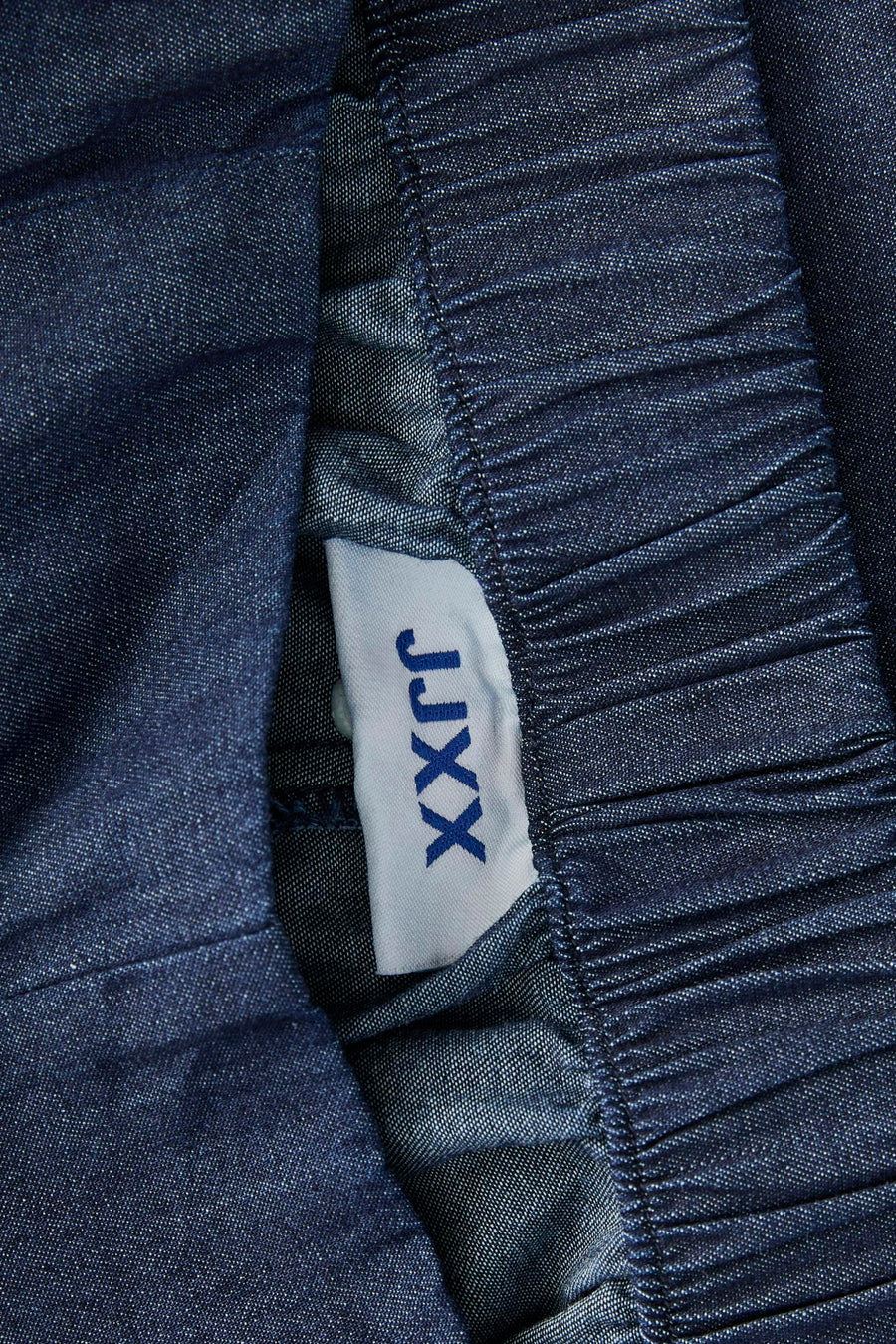 Donkerblauwe denim short van JJXX, detail van de gerimpelde taille en een wit merklabel.