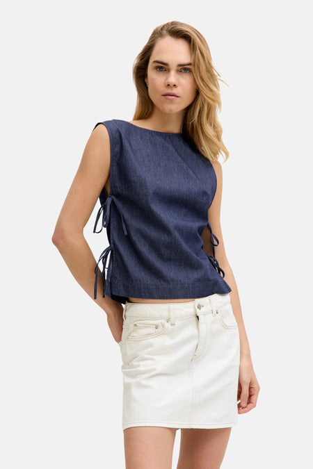 Donkerblauwe denim blouse van JJXX, mouwloos met strikdetails aan de zijkanten, gedragen met een witte spijkerrok.