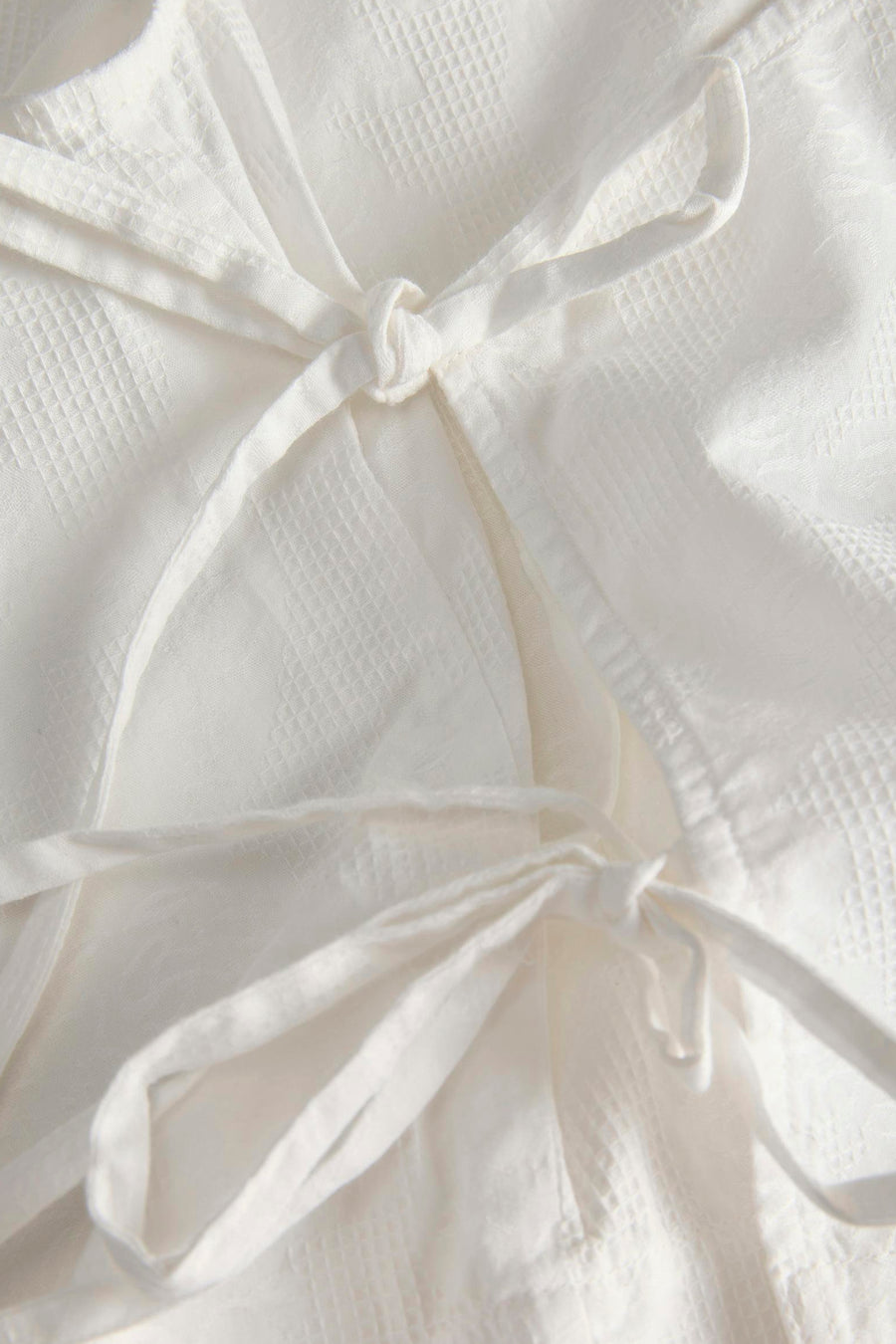 Witte blouse van JJXX met wafeltextuur en decoratieve strikjes.
