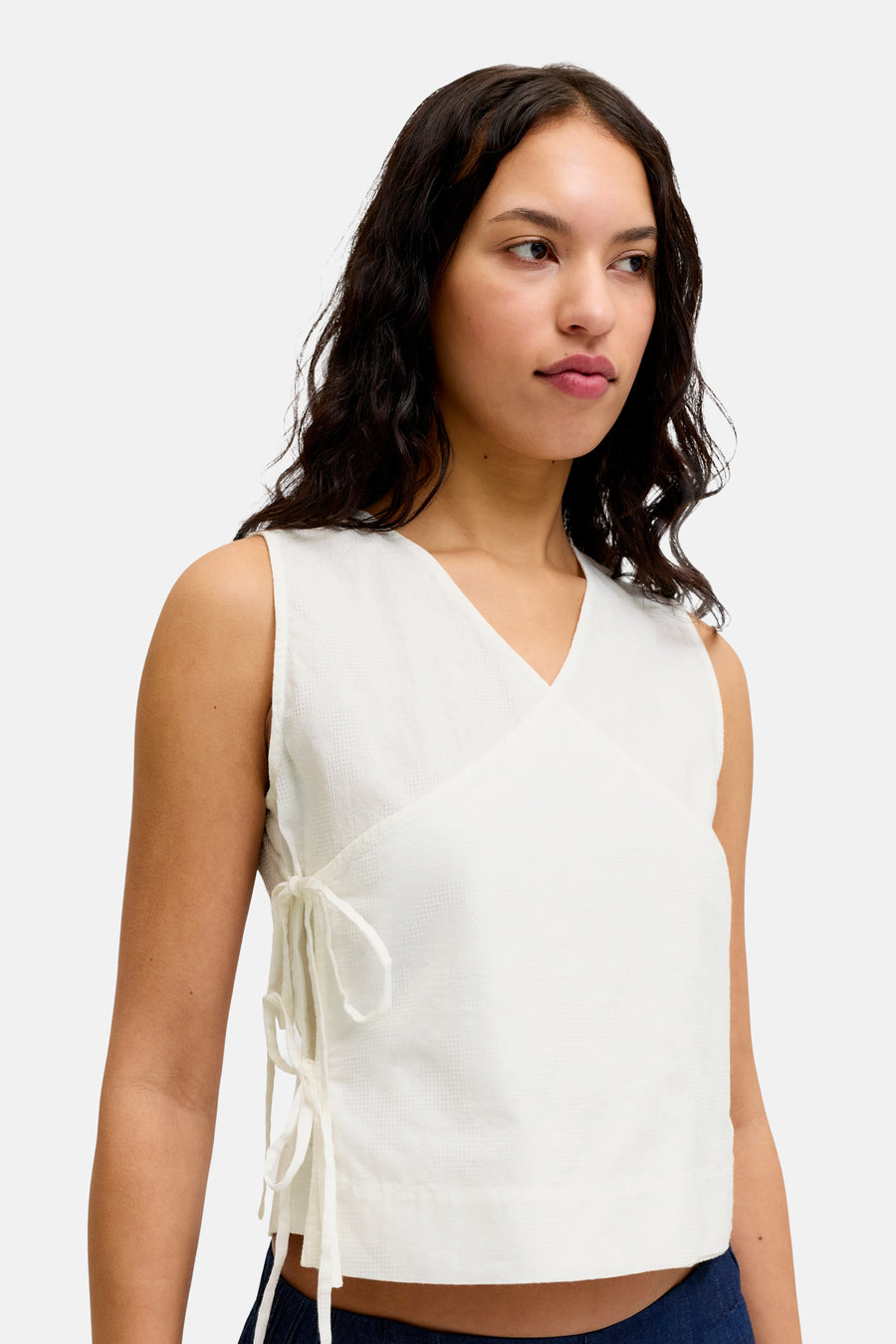 Witte blouse van JJXX, een mouwloos overslagmodel met subtiele weefstructuur en strikbandjes aan de zijkant.