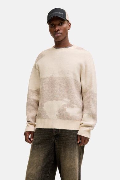 Beige trui met ronde hals van CORE BY JACK & JONES, met een abstract patroon en gedragen met donkere jeans en een pet.
