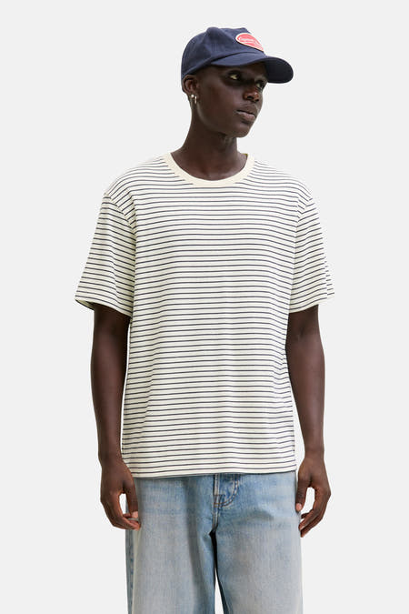 Beige T-shirt met korte mouwen van Originals by Jack & Jones, met zwarte horizontale strepen, gecombineerd met denim shorts en een pet.