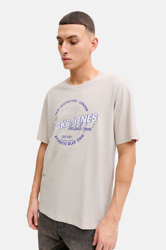 T-shirt beige à manches courtes d'ORIGINALS par JACK & JONES, avec une impression de texte bleue sur le devant et porté avec un jeans foncé.