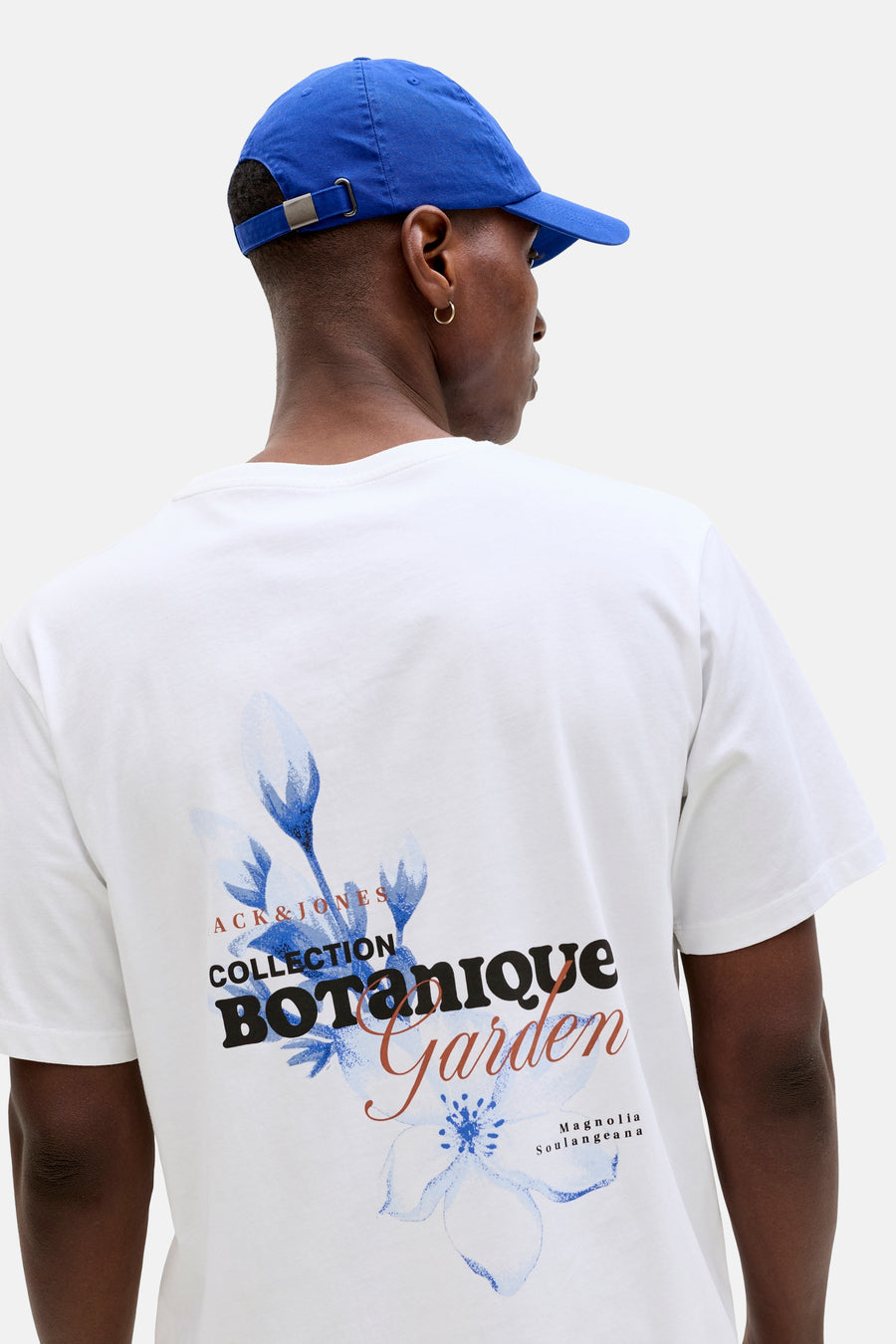 T-shirt blanc de ORIGINALS BY JACK & JONES, avec un imprimé botanique au dos et porté avec une casquette bleue.