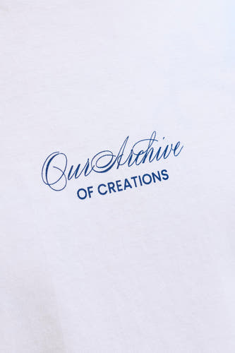 Wit T-shirt van ORIGINALS BY JACK & JONES met blauwe print 'Our Archive OF CREATIONS' op de witte stof, close-up.