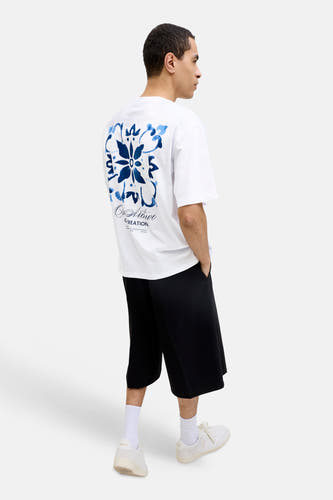 Wit T-shirt van ORIGINALS BY JACK & JONES met blauw bloemenpatroon en tekst op de rug, gedragen met zwarte shorts en sneakers.