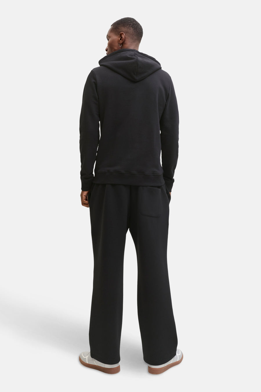 Zwarte sweater met kap van CORE BY JACK & JONES, gezien van achteren, met bijpassende zwarte broek en witte schoenen met bruine zolen.