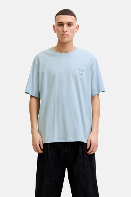 T-shirt bleu de ORIGINALS BY JACK & JONES avec imprimé discret sur la poitrine, porté avec un short foncé et des baskets blanches.