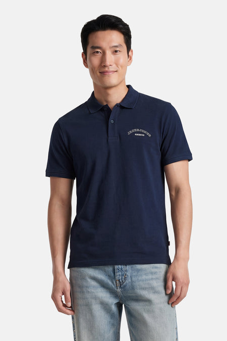 Polo bleue de ORIGINALS BY JACK & JONES à manches courtes avec un logo blanc sur la poitrine, portée par un homme souriant avec un jean clair.
