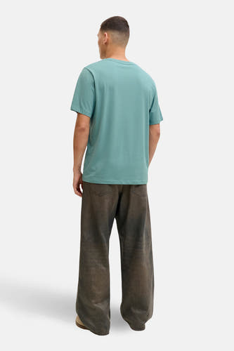 T-shirt bleu à manches courtes de CORE BY JACK & JONES, porté avec un dos nu, des pantalons marrons et des chaussures marrons.