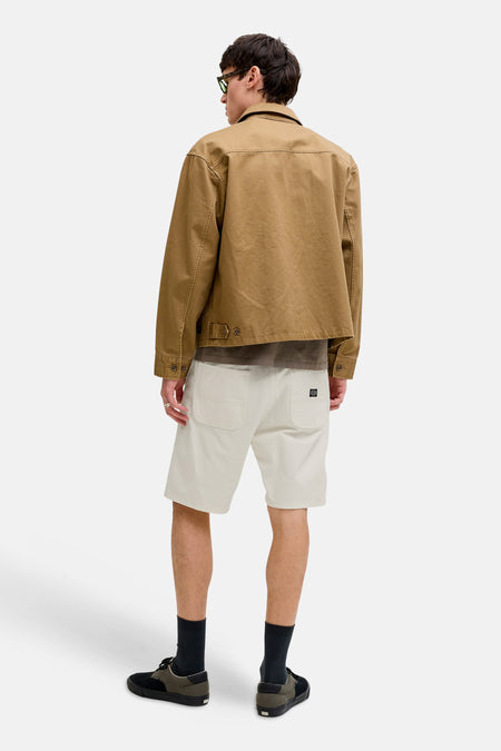 Beige short van JACK & JONES JEANS INTELLIGENCE, met achterzakken en een merklabel, gecombineerd met een bruine jas en zwarte sokken.