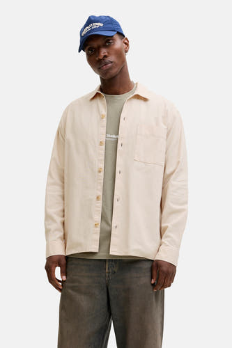Chemise beige à manches longues de ORIGINALS BY JACK & JONES, avec fermeture boutonnée et poche poitrine, portée sur un t-shirt vert et un jean foncé.