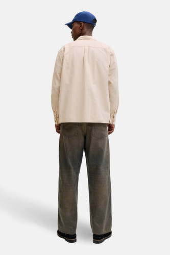 Chemise beige à manches longues de ORIGINALS by JACK & JONES, portée avec une casquette bleue et un jean foncé.