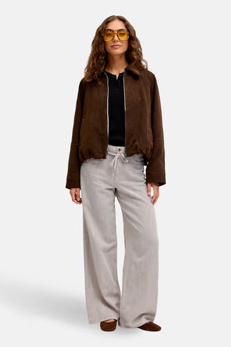 Beige broek van JJXX, met wijde pijpen en een trekkoord in de taille, gedragen met een bruin jasje en zwarte top.
