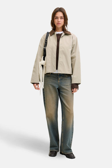 Manteau beige court de JJXX, avec un col marron et le modèle porte une veste marron et des jeans bleus.