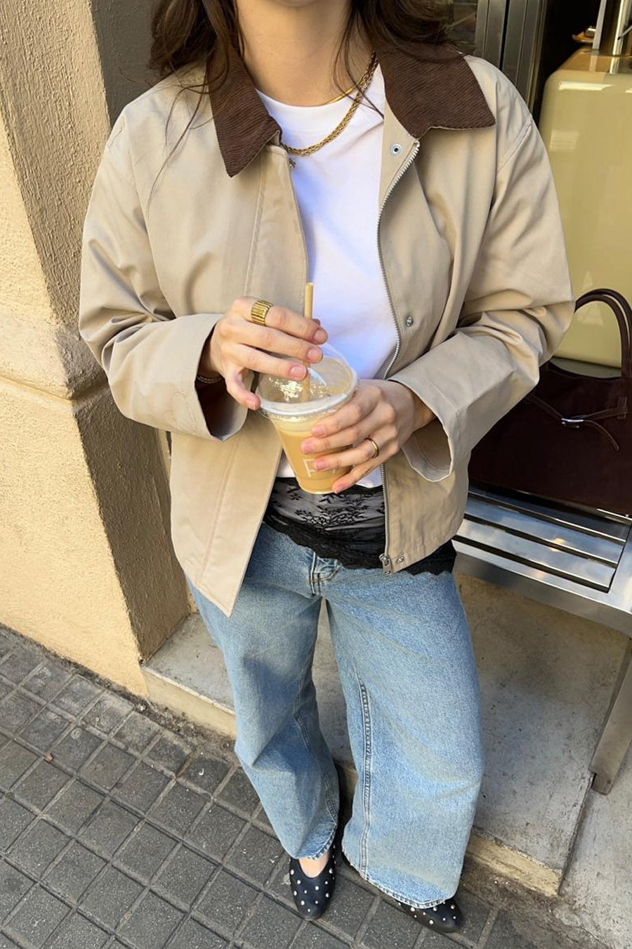 Beige korte jas van JJXX met bruine ribkraag, gedragen over een wit T-shirt en jeans, met een iced coffee in de hand.