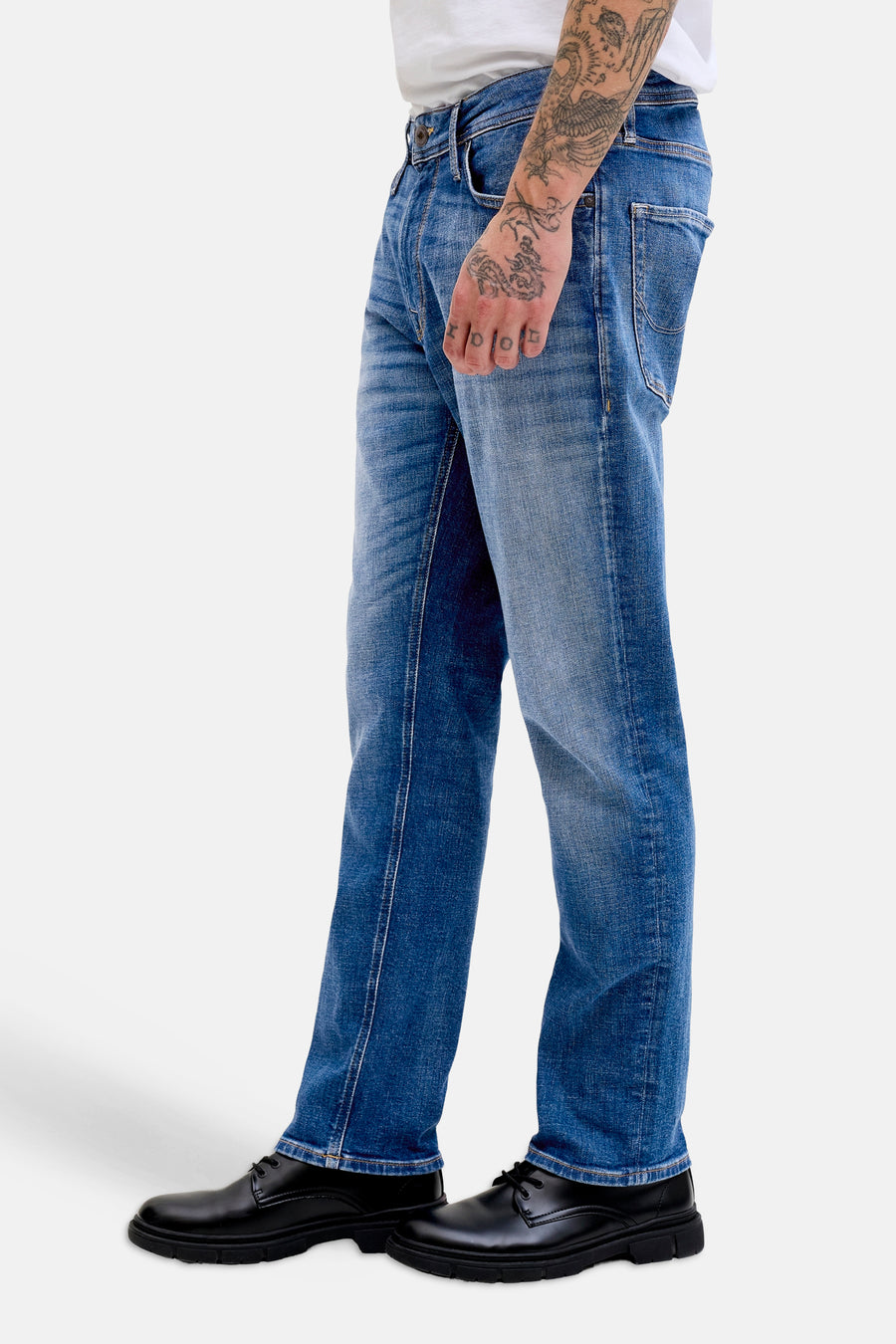 Middenblauwe rechte jeans van JACK & JONES JEANS INTELLIGENCE met een gedragen look, gecombineerd met zwarte schoenen en een getatoeëerde arm.