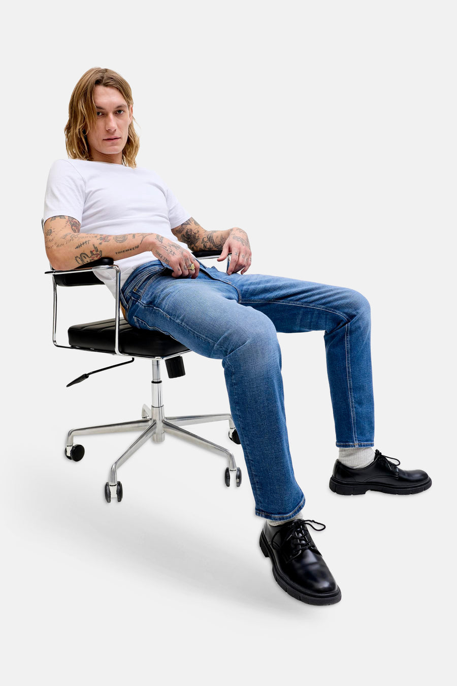 Mid blauwe denim rechte jeans van JACK & JONES JEANS INTELLIGENCE, gedragen door een zittende man met wit T-shirt en zwarte schoenen.
