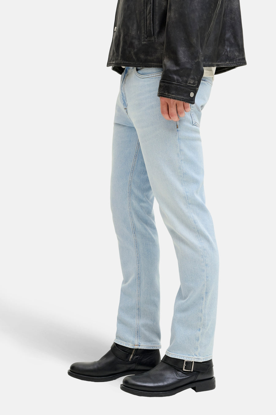 Man, staand, leren jack, lichte jeans, zwarte laarzen.
