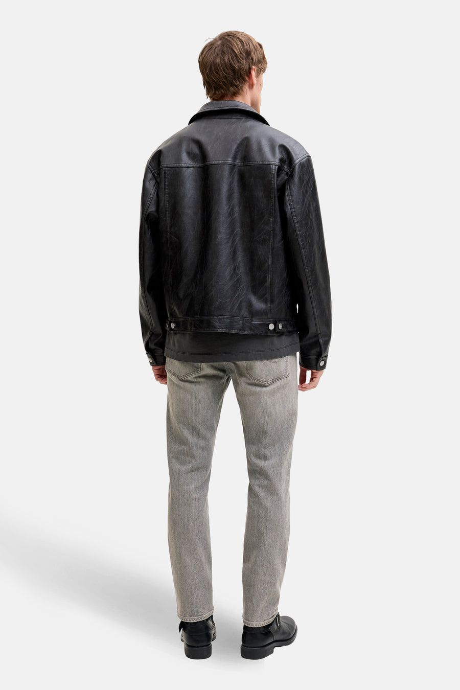 Man van achteren in een zwarte leren jas en grijze jeans.