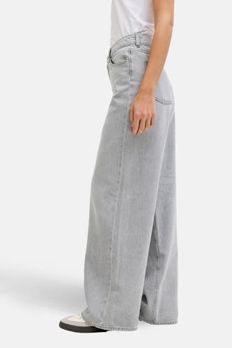 Lichtgrijze, wijde jeans van JJXX, met een denim textuur, gedragen met een wit T-shirt en sneakers, in zijaanzicht.
