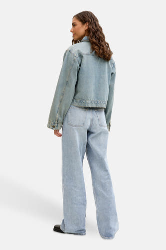 Lichtblauwe wijde jeans van JJXX, gezien van achteren met een bijpassend denim jack en zwarte schoenen.