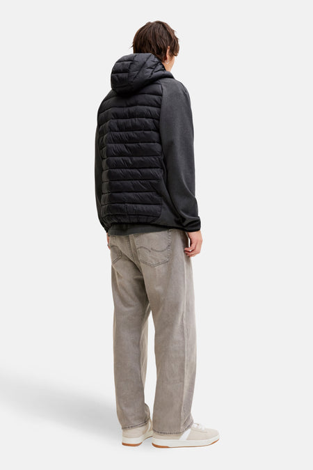 Achteraanzicht van een man in een grijs sweatshirt met een zwart pufferjack met capuchon, grijze jeans en beige sneakers.