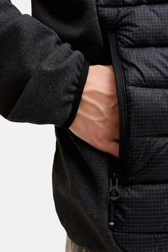 Persoon steekt hand in zak van zwart pufferjack met ruitjespatroon.