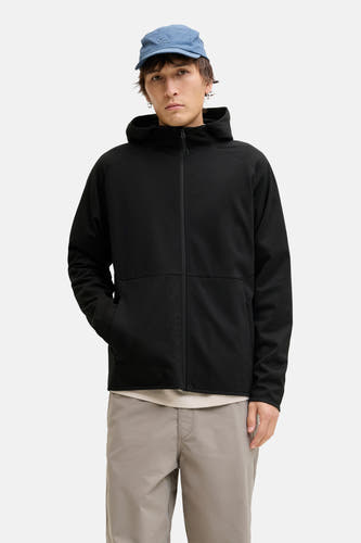 Zwarte sweater gilet van CORE BY JACK & JONES, met lange mouwen en een capuchon, gecombineerd met een blauwe pet en grijze broek.

