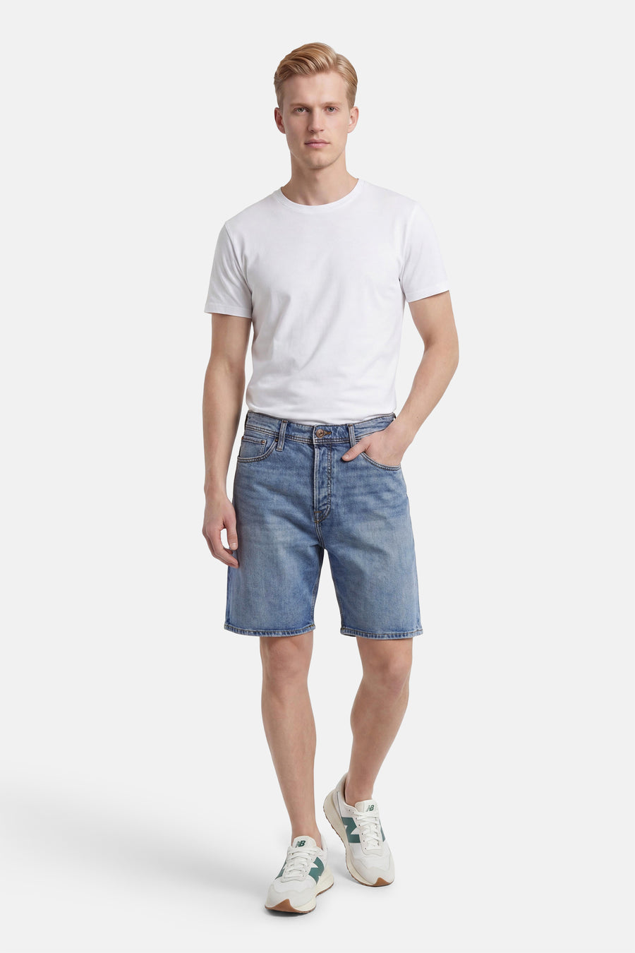 Mid-blauwe jeansshort van JACK & JONES JEANS INTELLIGENCE met knoopsluiting, gedragen door een man met wit T-shirt en sneakers.