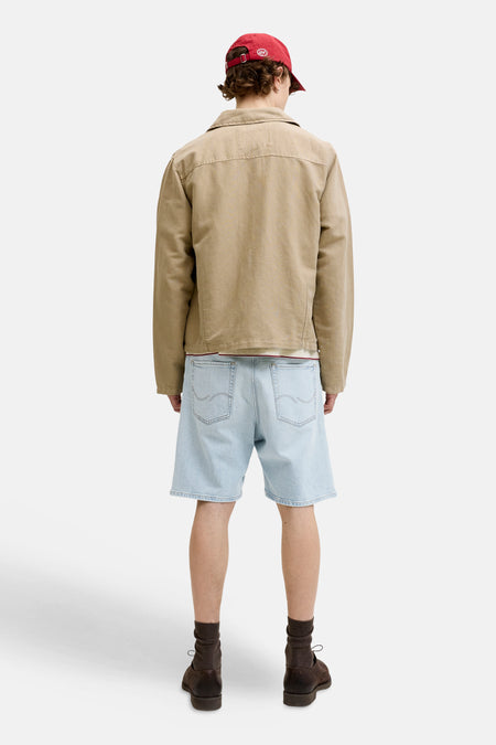 Jeansshort van lichtblauw denim van Jack & Jones Jeans Intelligence, gezien van achteren, met bruine schoenen en sokken, en een beige jasje.