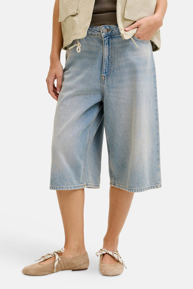 Korte lichtblauwe denim short van JJXX, met een wijde pijp en gecombineerd met beige schoenen en vest.
