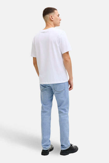 Man, staand, wit T-shirt, lichtblauwe jeans, zwarte schoenen.
