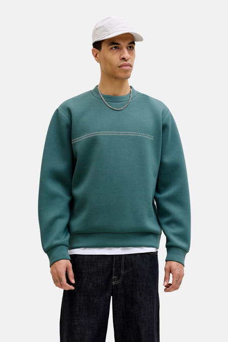 Pull bleu à col rond de CORE BY JACK & JONES, avec des rayures horizontales et combiné avec un jean ample et une casquette.